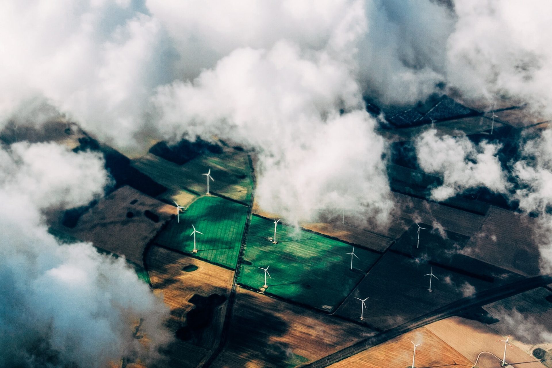 Eine Aufnahme aus dem Flugzeug, Wolken ziehen über Windräder, die auf Feldern stehen.